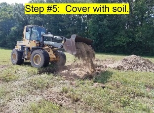  An Image of a payloader placing soil on top of the above ground burial trench.