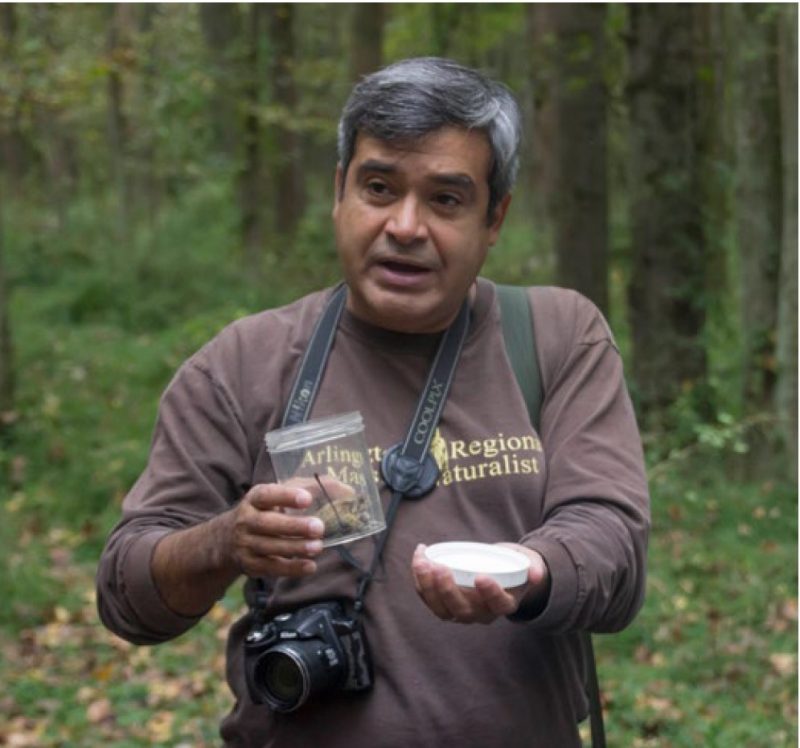 An instructor, with a camera hanging from his neck, holds a jar with something inside.