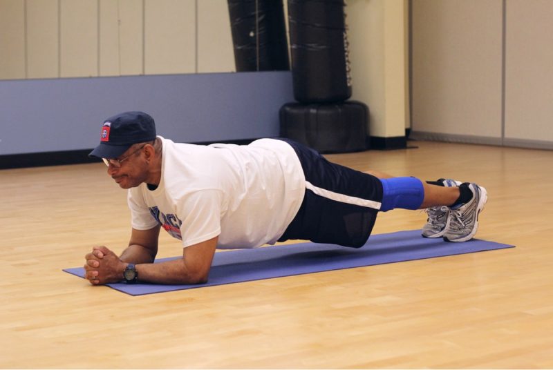 A man Lying on the ground with the elbows in line with the shoulder and the feet shoulder width apart. he is pushing his body up bearing the weight on  the forearms and feet, Keeping his body straight.