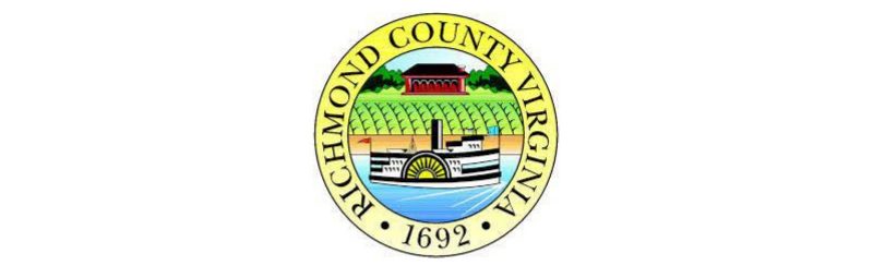 County seal of Richmond County, Virginia. Circle outlined in yellow with red building, green crops and steam boat in center.
