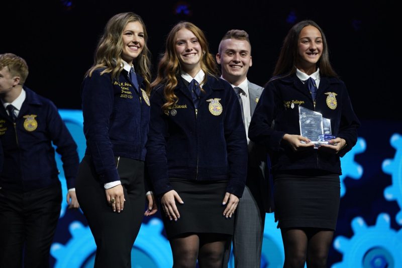 Three smiling FFA female students hold an award.