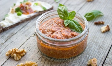 a photo of tomato-based pesto in a glass container on a table
