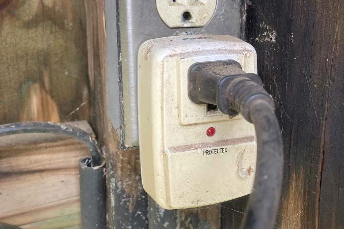 A single-outlet surge protector plugged into an outlet, with the cord of an energizer plugged into the surge protector.